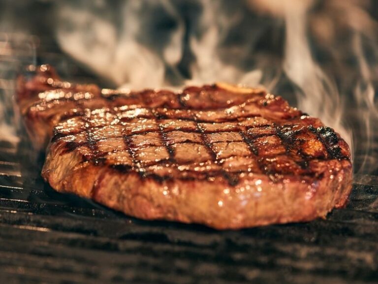 Closeup of a steak cooking on a griddle.