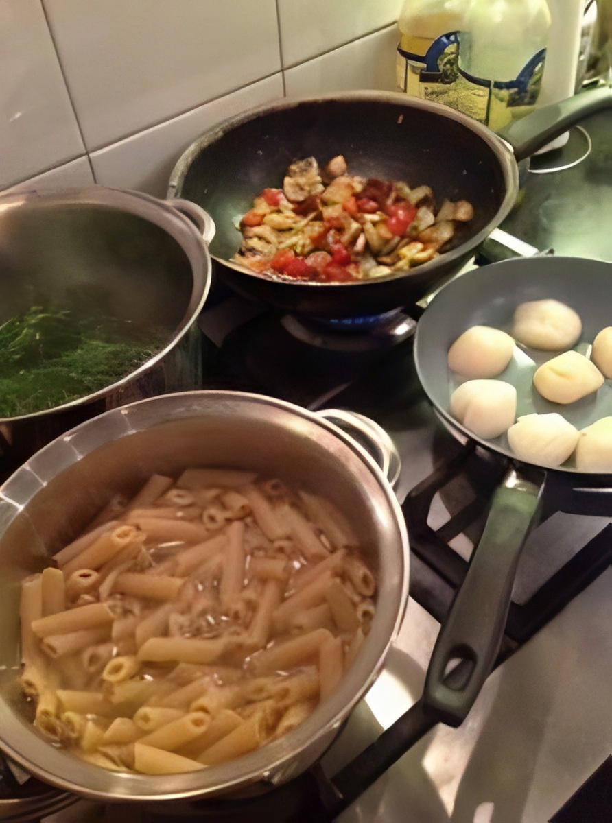 Pasta, scallops and vegetables cooking in separate pans on the stove