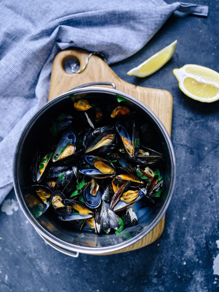 Steamed mussels with parsley in a pot beside lemon wedges