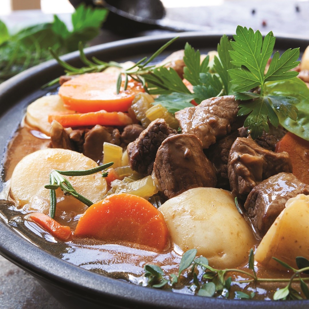 Irish lamb stew with potatoes, sliced carrots and fresh herbs in a black bowl.