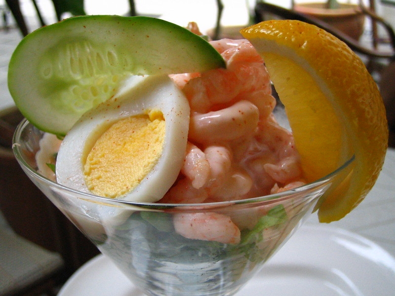 A glass of prawn cocktail with orange and egg garnishes.