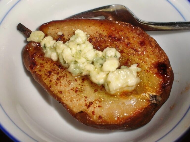 A pear half filled with blue cheese on a white serving plate.