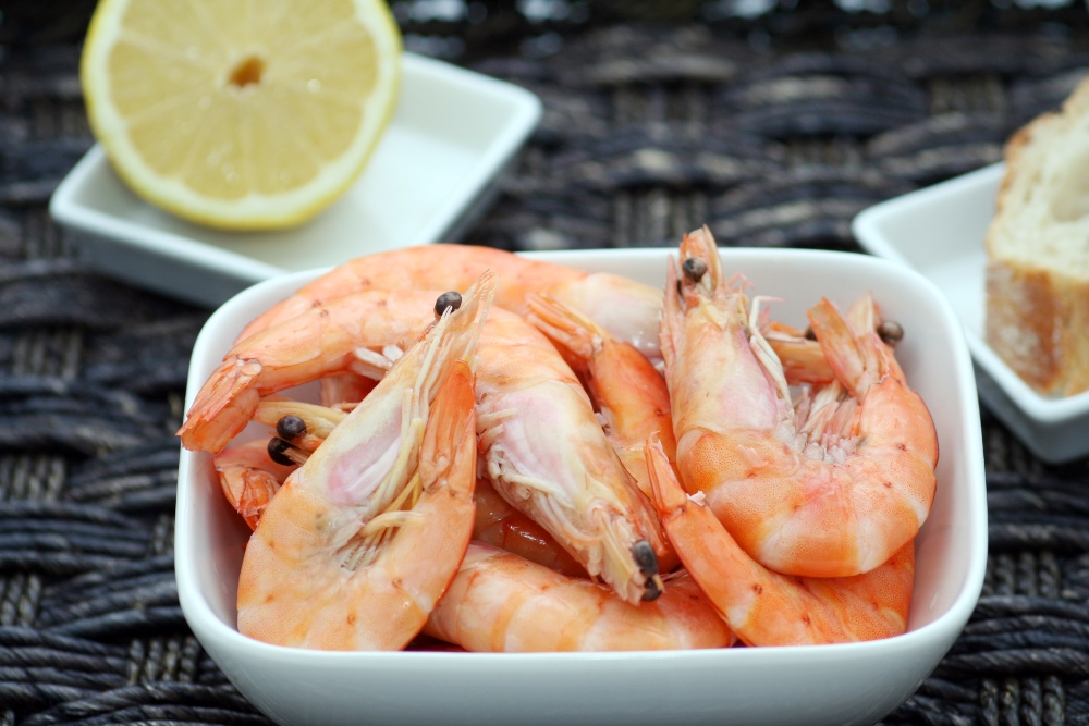 Shell-on prawns in a white dish with half a lemon in the background.