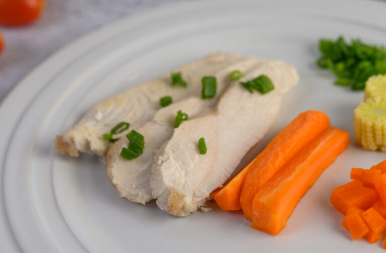 Steamed chicken breast on a plate with fresh herbs and vegetables.