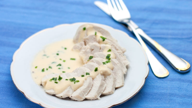 Sliced chicken breast with a cream sauce and fresh herbs.