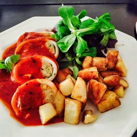 Sliced stuffed squid in tomato sauce with roasted potatoes and salad greens