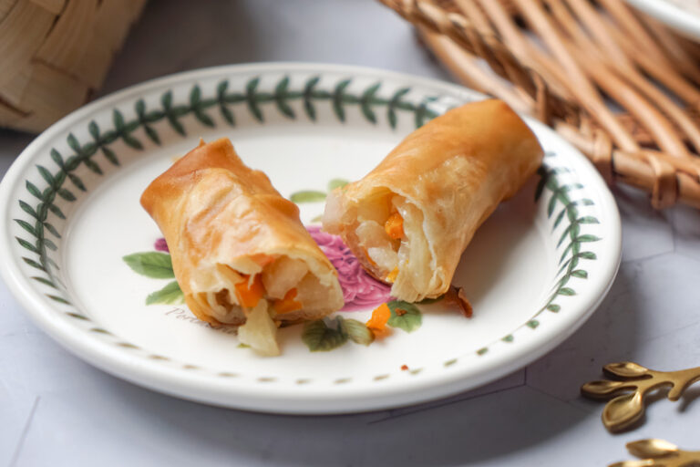 A fried Malaysian popiah spring roll cut open on a plate, to show the vegetable filling.