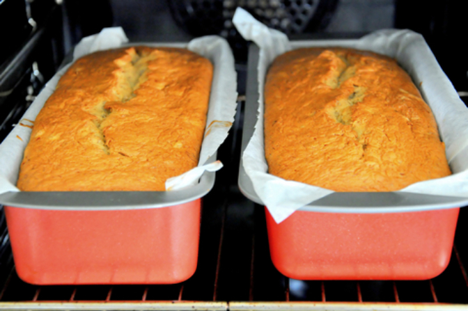 Two golden banana bread loaves in parchment-lined red loaf pans.