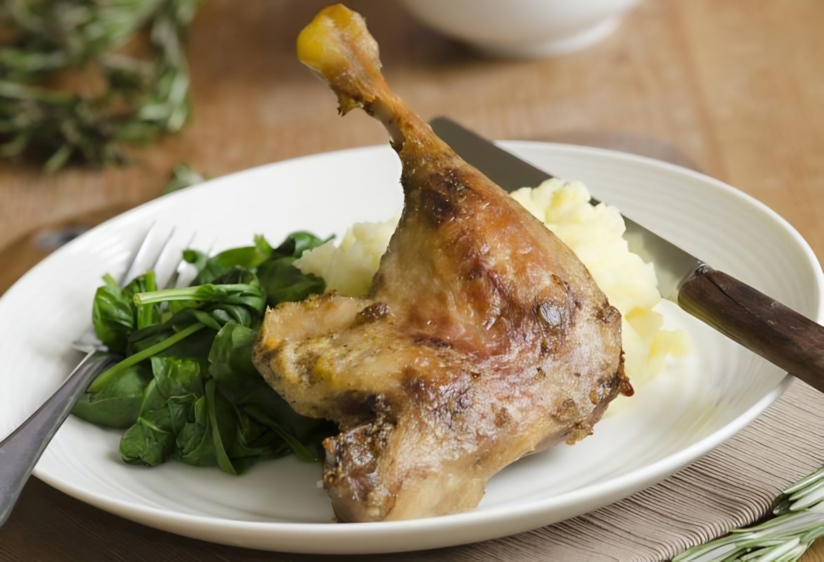 Roasted duck leg with mashed potatoes and spinach on a white plate.