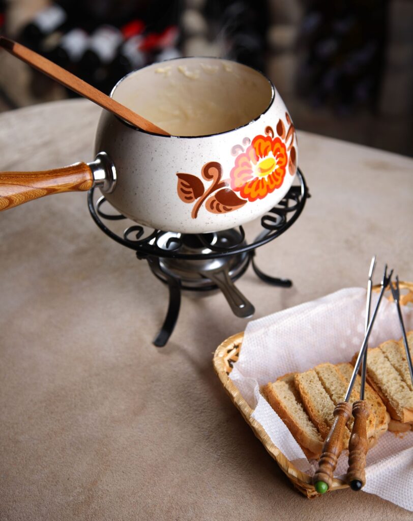 Cheese fondue in a vintage fondue pot with bread cubes and fondue forks.