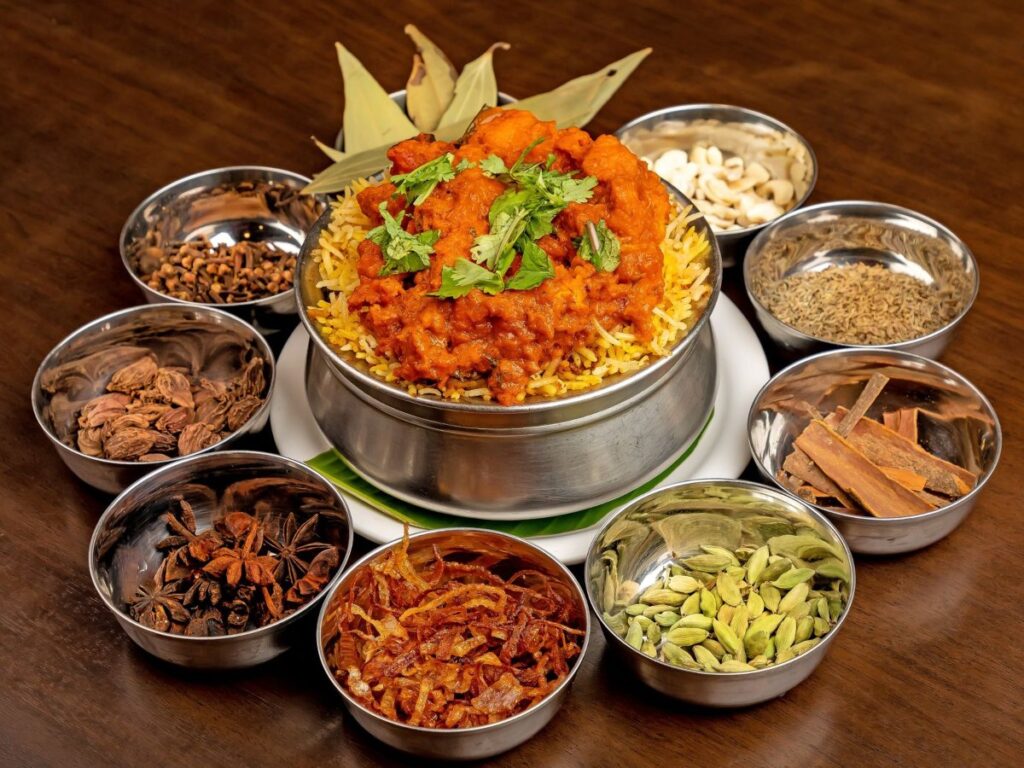 Biryani with a cilantro and curry leaf garnish and small bowls of spices all around.