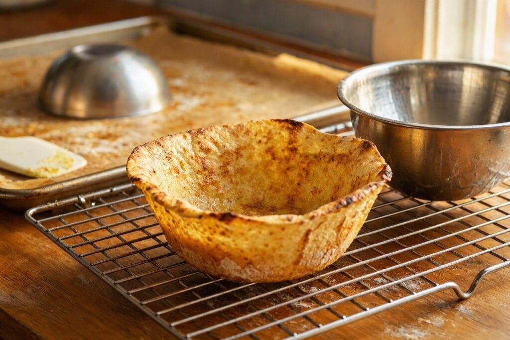 A crisp tortilla bowl on a cooling rack next to a metal bowl mold.