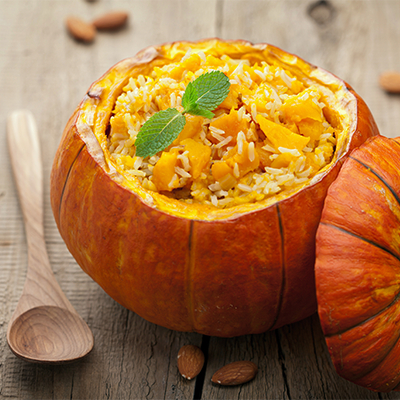 Pumpkin risotto topped with mint in a hollowed pumpkin, with the lid beside it.