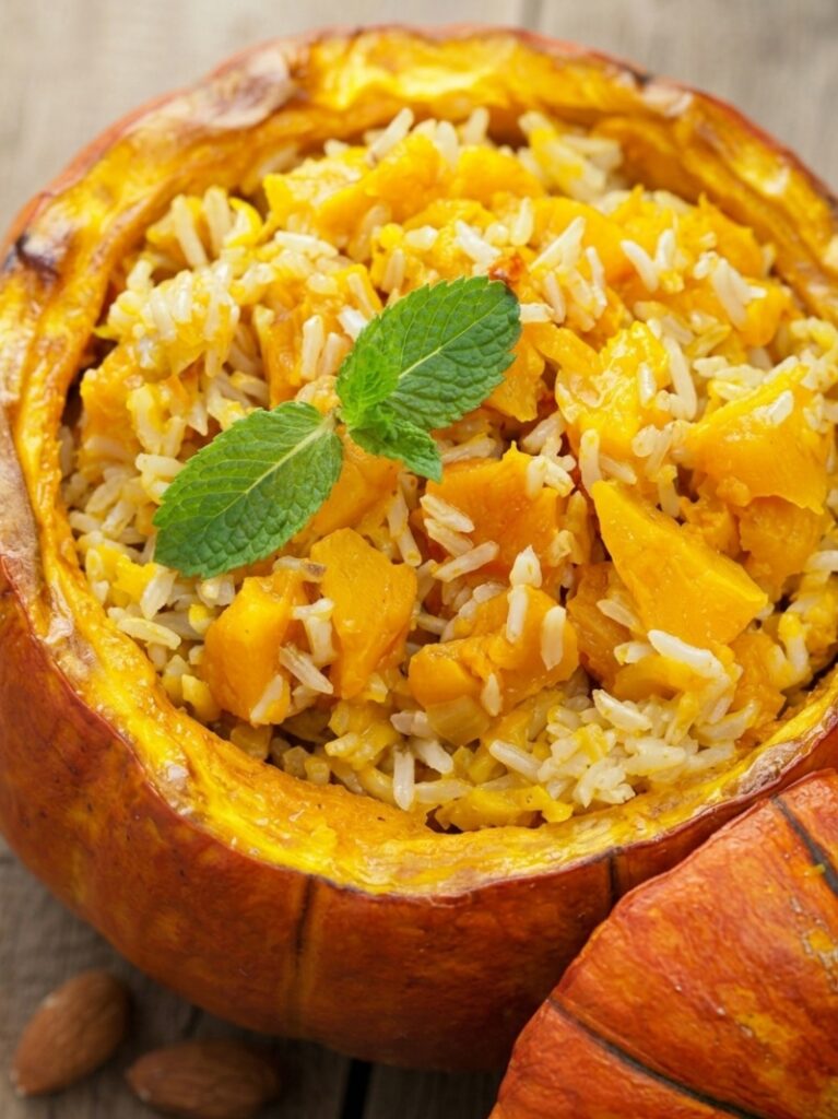 Close-up of pumpkin risotto with pumpkin pieces and mint leaves in a hollowed pumpkin.