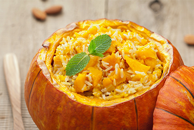 Pumpkin risotto topped with fresh mint in a hollowed pumpkin, with the lid beside it.