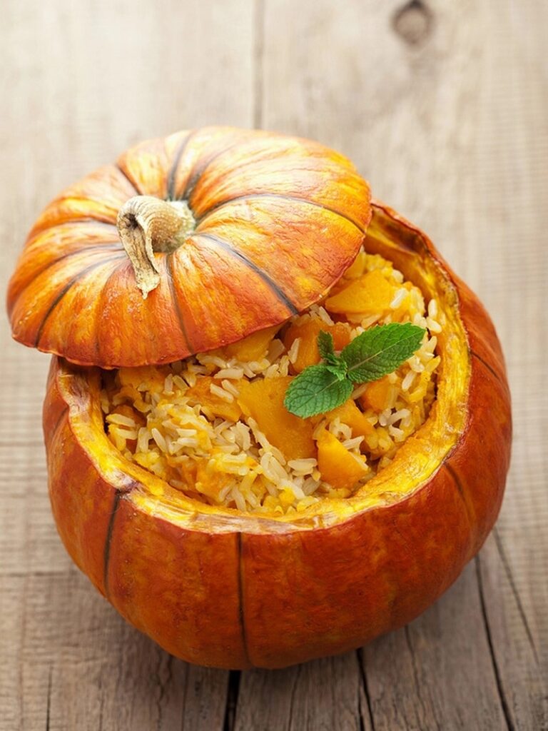 Pumpkin risotto topped with mint in a hollowed pumpkin, with the lid resting on the rim.