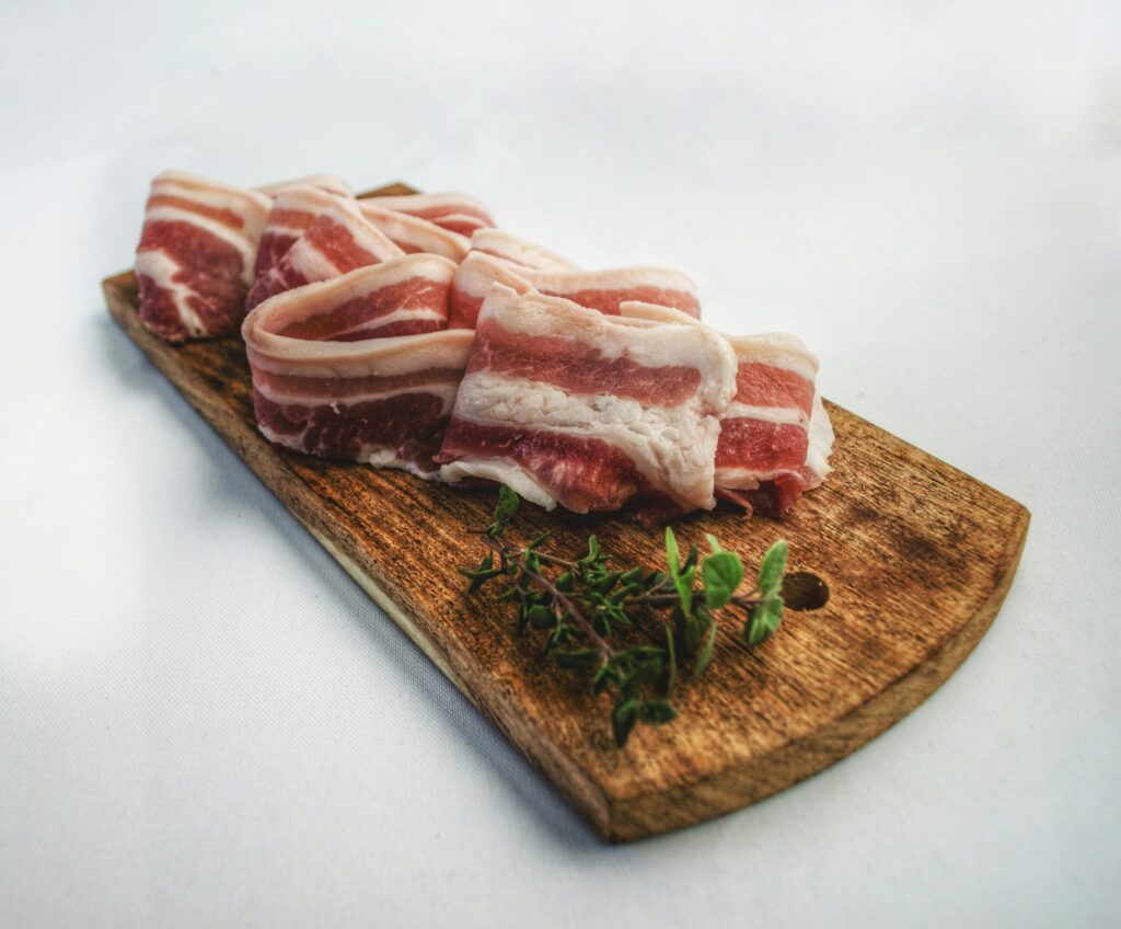 Raw pork belly strips, speklappen, on a wooden cutting board.