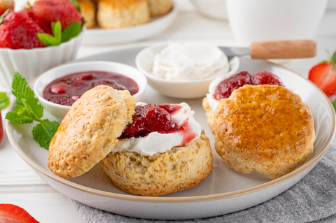 Scones with jam and clotted cream on a white plate with a fresh mint garnish.