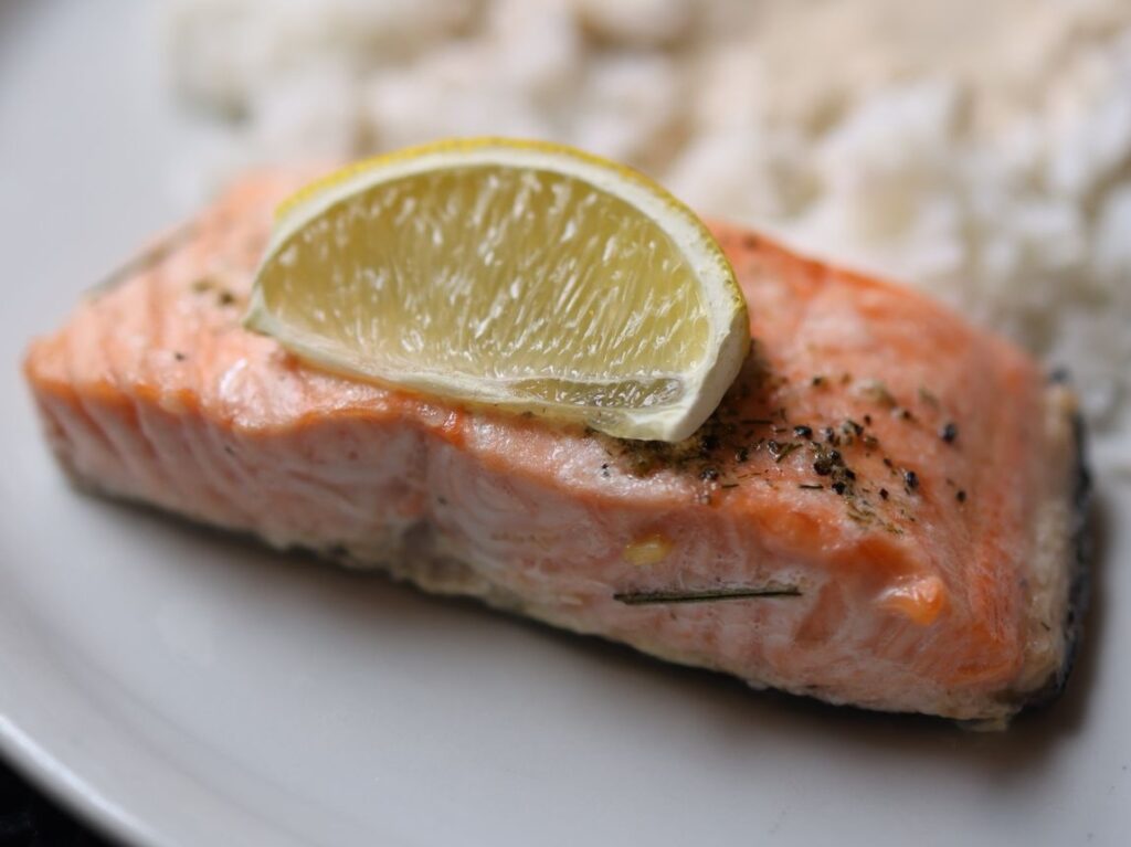 Smoked salmon on a plate with a lemon wedge on top.