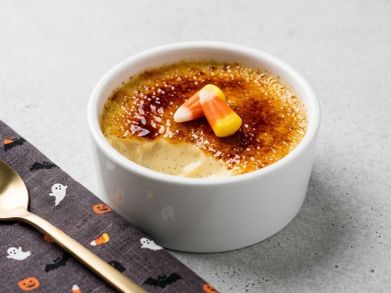 A bowl of creme brulee candy corn dessert with a Halloween napkin and spoon on the side.