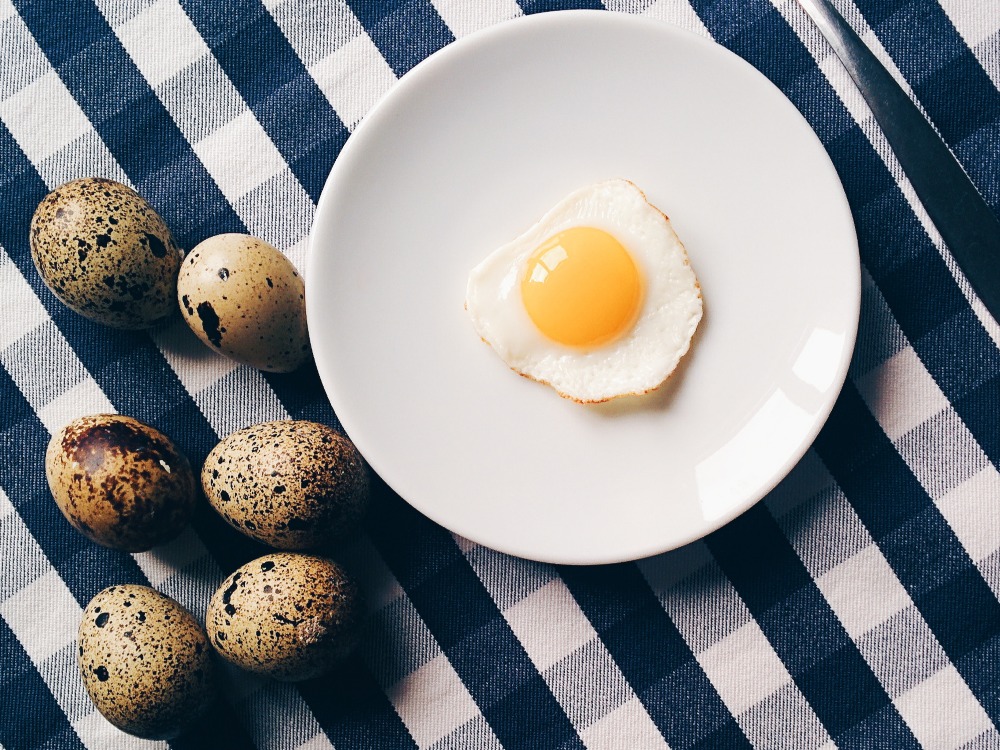 A cooked quail egg on a plate with some uncooked eggs on the side.