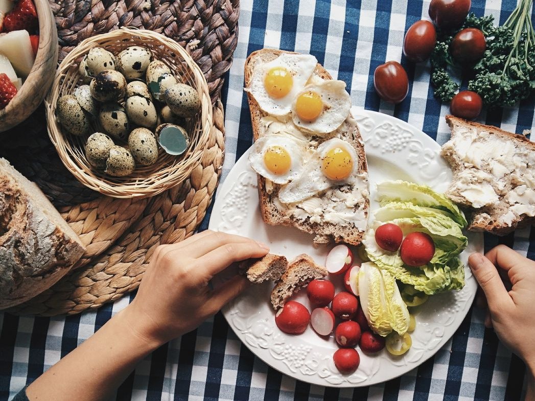 Four fried quail eggs on toast with radishes, lettuce and a basket of speckled eggs