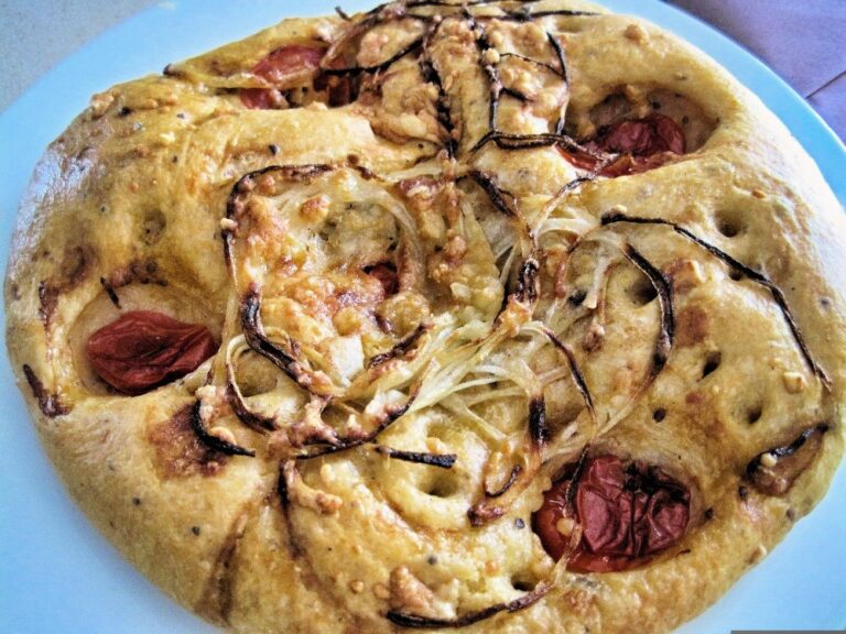 Round focaccia topped with roasted tomatoes and sliced onion on a blue plate