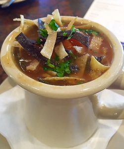 A bowl of chicken tortilla soup with crispy tortilla strips on top.