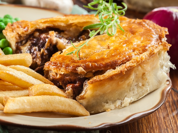Individual beef pie cut open beside fries and peas.