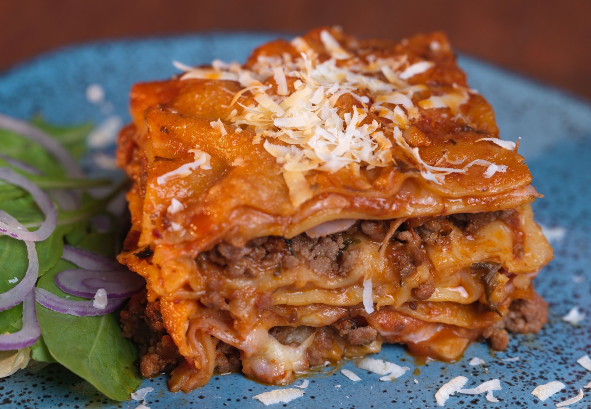A slice of Ronzoni lasagna on a blue plate.
