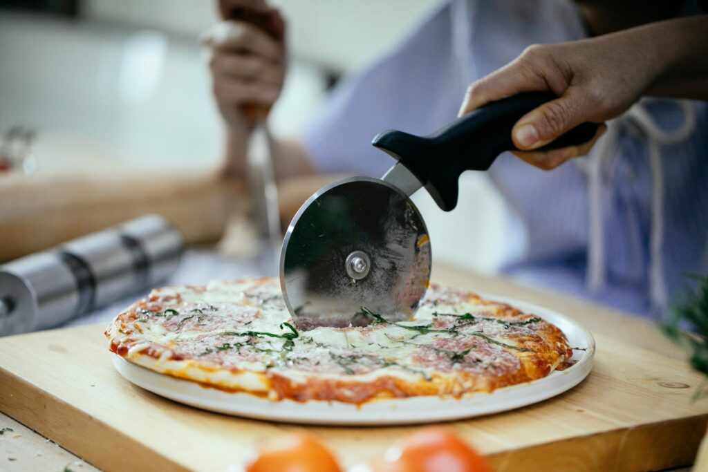 Slicing a cooked pizza with a pizza wheel.