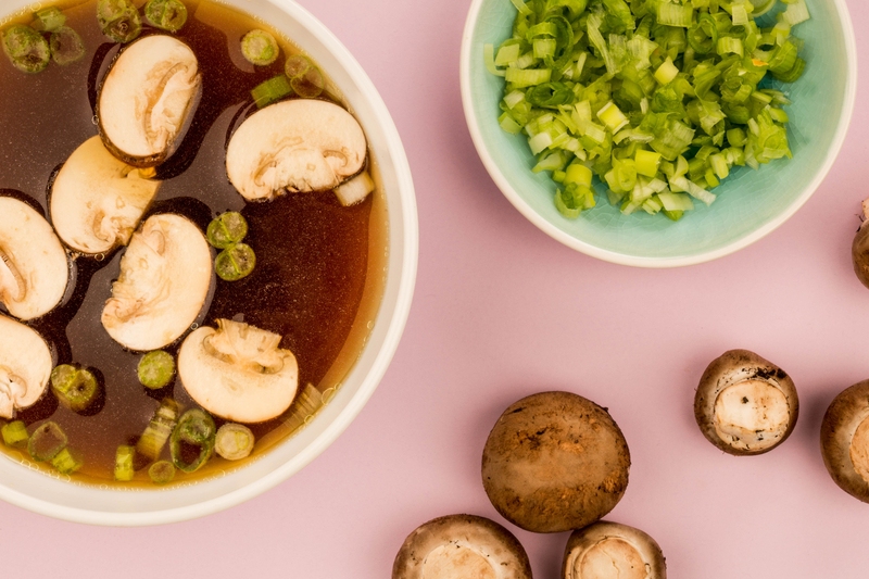 A bowl of Japanese onion soup with green onions and mushrooms on the side.