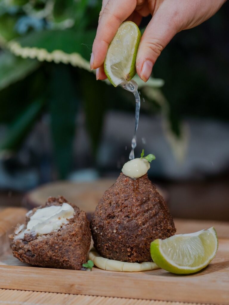 A person squeezing fresh lime juice over kibbeh.