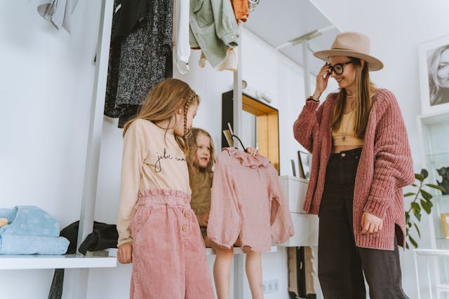 Woman showing clothes to two young children in a bright room while organizing a wardrobe