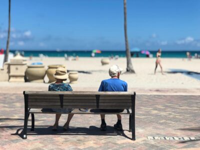 An older couple sitting on a bench on the beach