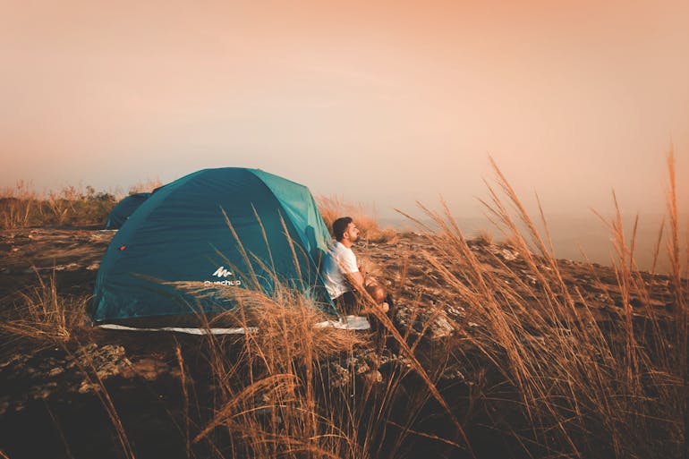 a man sitting in front of the tent thinking about the psychology of glamping