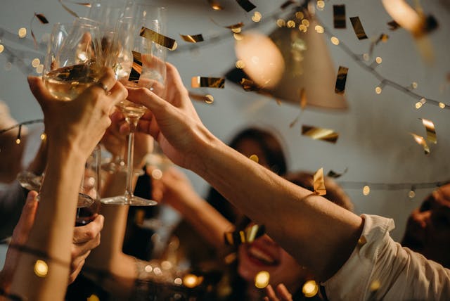 Close-up of people toasting with wine glasses, golden confetti falling