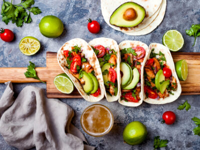 A wooden board with chicken avocado tacos and lime wedges