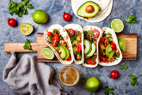 A wooden board with chicken avocado tacos and lime wedges