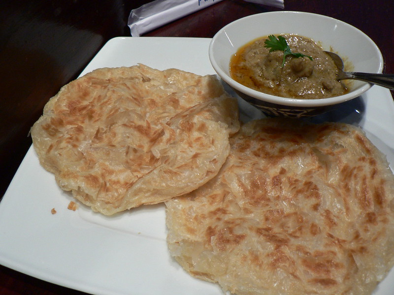 Roti canai on a white plate with a bowl of curry for dipping.