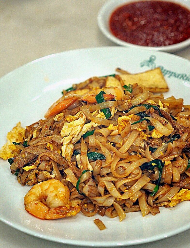 A plate of char kway teow with sauce in the background.