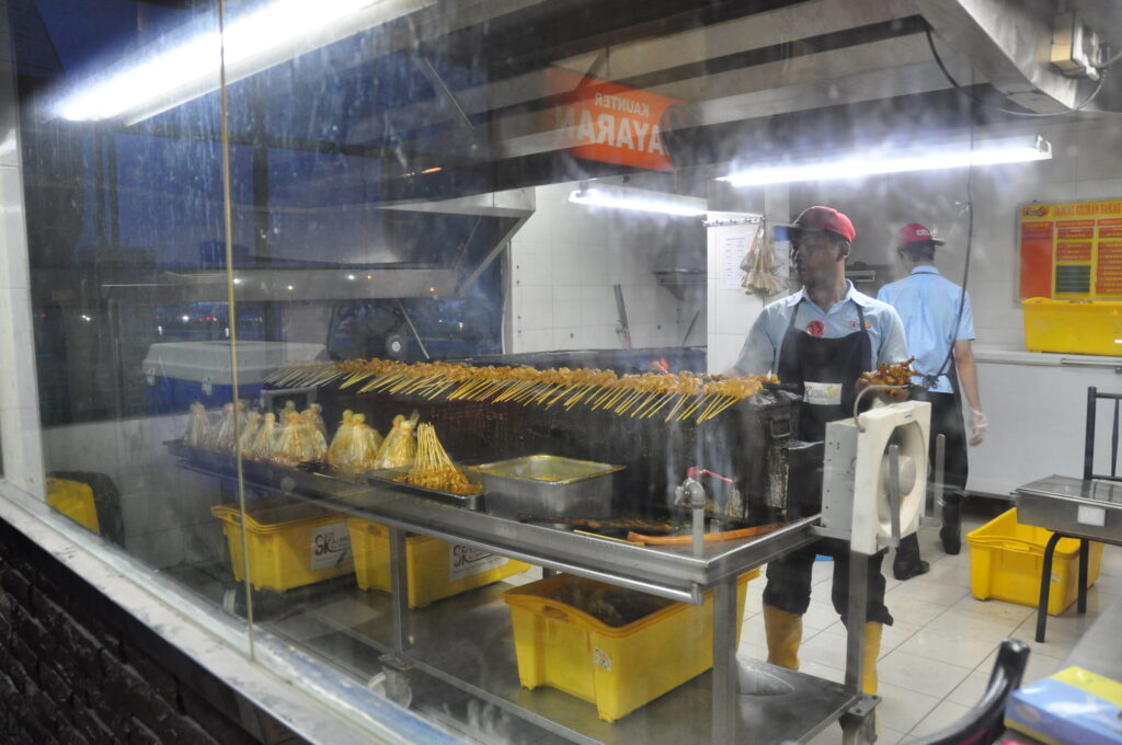 A Malaysian chef grilling satay in a large kitchen.