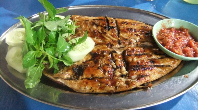 Malaysian grilled fish, known as Ikan Bakar, on a platter with a herb and cucumber garnish.