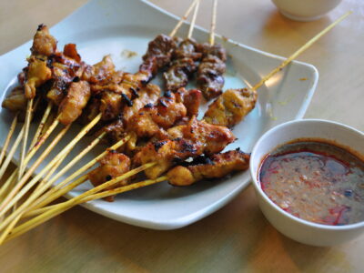 Malaysian chicken and beef satay skewers served with peanut dipping sauce on a plate.