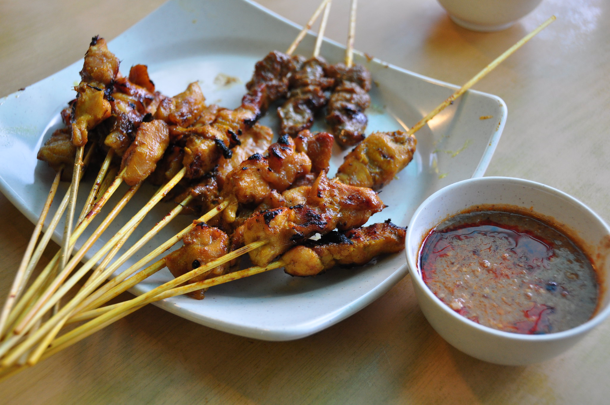 Malaysian chicken and beef satay skewers served with peanut dipping sauce on a plate.