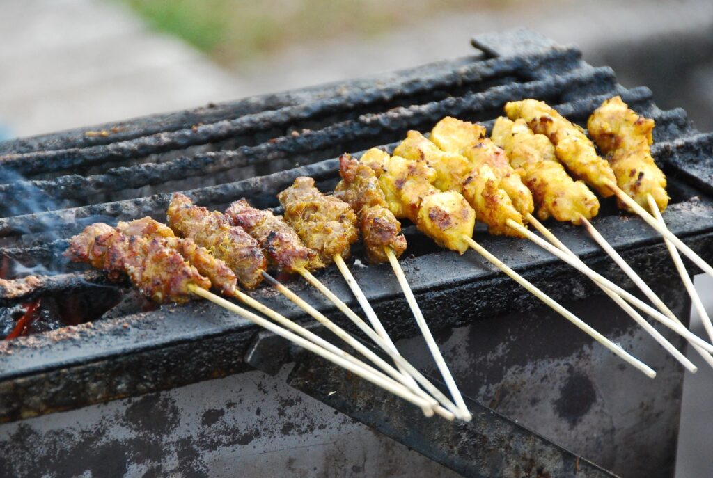 Sticks of Malaysian satay cooking on the grill.