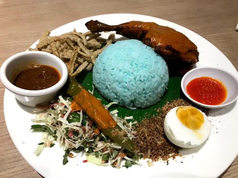 A plate of nasi kerabu, a Malaysian dish, served with garnishes and condiments.