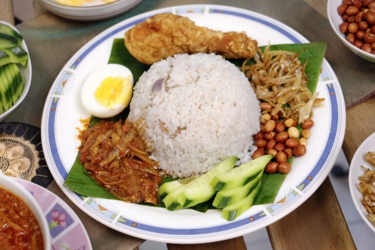 Close view of nasi lemak with coconut rice, sambal, crispy anchovies, peanuts, boiled egg and cucumber.