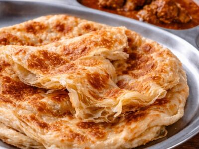 Malaysian roti canai on a metal platter with curry in the background.