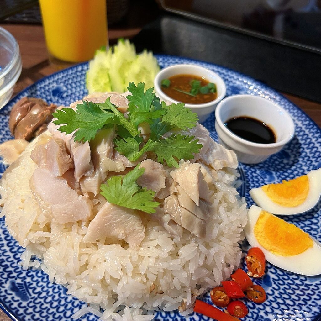 Plated chicken and rice with boiled egg, 2 sauces and cucumber garnish.